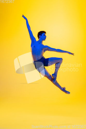 Image of Young and graceful ballet dancer isolated on yellow studio background in neon light. Art, motion, action, flexibility, inspiration concept.