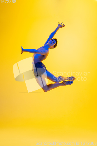 Image of Young and graceful ballet dancer isolated on yellow studio background in neon light. Art, motion, action, flexibility, inspiration concept.