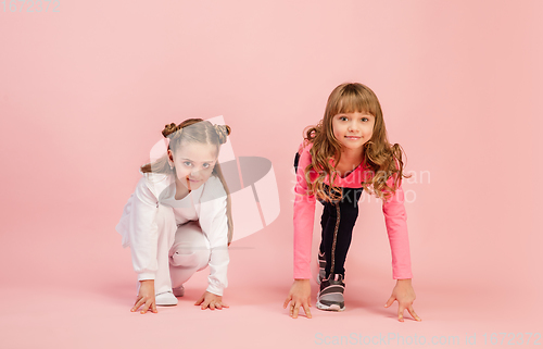 Image of Happy kids, girls isolated on coral pink studio background. Look happy, cheerful, sincere. Copyspace. Childhood, education, emotions concept