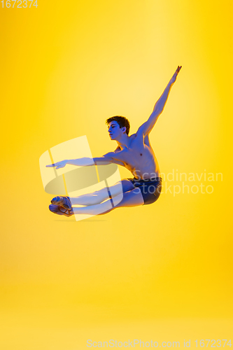 Image of Young and graceful ballet dancer isolated on yellow studio background in neon light. Art, motion, action, flexibility, inspiration concept.