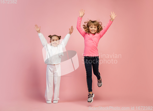 Image of Happy kids, girls isolated on coral pink studio background. Look happy, cheerful, sincere. Copyspace. Childhood, education, emotions concept