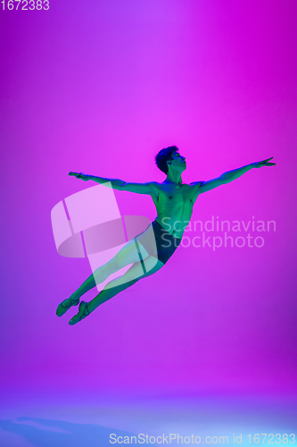 Image of Young and graceful ballet dancer isolated on purple studio background in neon light. Art, motion, action, flexibility, inspiration concept.