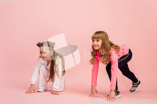 Image of Happy kids, girls isolated on coral pink studio background. Look happy, cheerful, sincere. Copyspace. Childhood, education, emotions concept