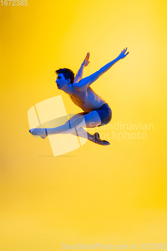 Image of Young and graceful ballet dancer isolated on yellow studio background in neon light. Art, motion, action, flexibility, inspiration concept.
