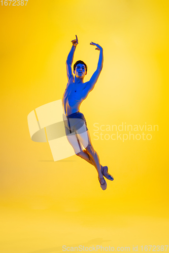 Image of Young and graceful ballet dancer isolated on yellow studio background in neon light. Art, motion, action, flexibility, inspiration concept.