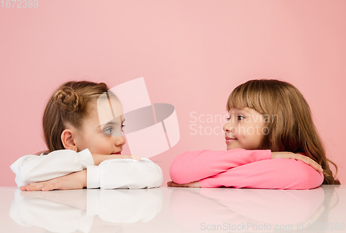 Image of Happy kids, girls isolated on coral pink studio background. Look happy, cheerful, sincere. Copyspace. Childhood, education, emotions concept