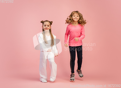 Image of Happy kids, girls isolated on coral pink studio background. Look happy, cheerful, sincere. Copyspace. Childhood, education, emotions concept