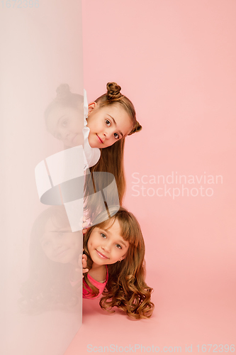 Image of Happy kids, girls isolated on coral pink studio background. Look happy, cheerful, sincere. Copyspace. Childhood, education, emotions concept