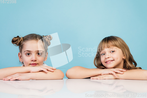 Image of Happy kids, girls isolated on blue studio background. Look happy, cheerful, sincere. Copyspace. Childhood, education, emotions concept