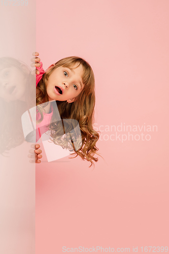 Image of Happy kid, girl isolated on coral pink studio background. Looks happy, cheerful, sincere. Copyspace. Childhood, education, emotions concept