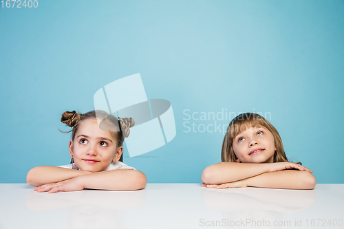 Image of Happy kids, girls isolated on blue studio background. Look happy, cheerful, sincere. Copyspace. Childhood, education, emotions concept