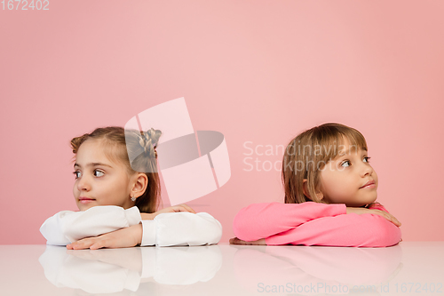 Image of Happy kids, girls isolated on coral pink studio background. Look happy, cheerful, sincere. Copyspace. Childhood, education, emotions concept