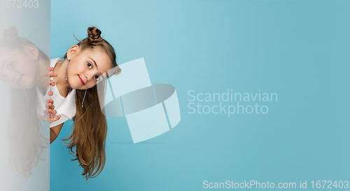 Image of Happy kid, girl isolated on blue studio background. Looks happy, cheerful, sincere. Copyspace. Childhood, education, emotions concept