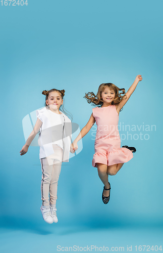Image of Happy kids, girls isolated on blue studio background. Look happy, cheerful, sincere. Copyspace. Childhood, education, emotions concept