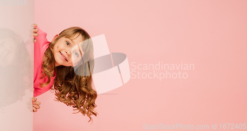 Image of Happy kid, girl isolated on coral pink studio background. Looks happy, cheerful, sincere. Copyspace. Childhood, education, emotions concept