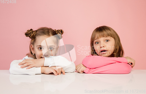 Image of Happy kids, girls isolated on coral pink studio background. Look happy, cheerful, sincere. Copyspace. Childhood, education, emotions concept