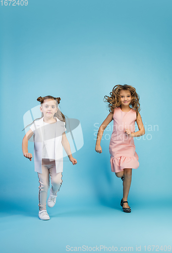 Image of Happy kids, girls isolated on blue studio background. Look happy, cheerful, sincere. Copyspace. Childhood, education, emotions concept