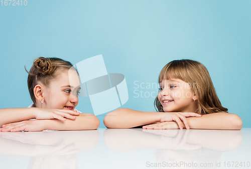 Image of Happy kids, girls isolated on blue studio background. Look happy, cheerful, sincere. Copyspace. Childhood, education, emotions concept