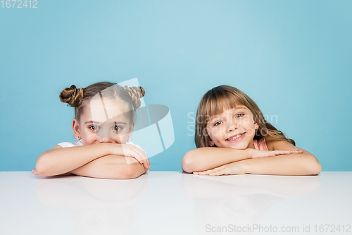 Image of Happy kids, girls isolated on blue studio background. Look happy, cheerful, sincere. Copyspace. Childhood, education, emotions concept