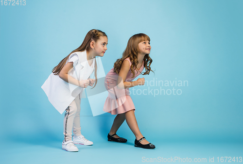 Image of Happy kids, girls isolated on blue studio background. Look happy, cheerful, sincere. Copyspace. Childhood, education, emotions concept