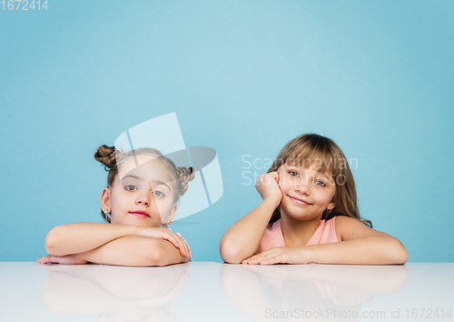 Image of Happy kids, girls isolated on blue studio background. Look happy, cheerful, sincere. Copyspace. Childhood, education, emotions concept