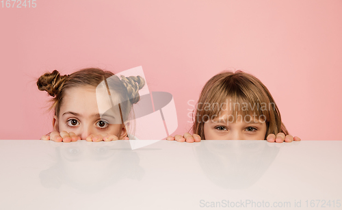 Image of Happy kids, girls isolated on coral pink studio background. Look happy, cheerful, sincere. Copyspace. Childhood, education, emotions concept