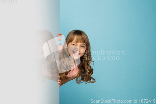 Image of Happy kid, girl isolated on blue studio background. Looks happy, cheerful, sincere. Copyspace. Childhood, education, emotions concept