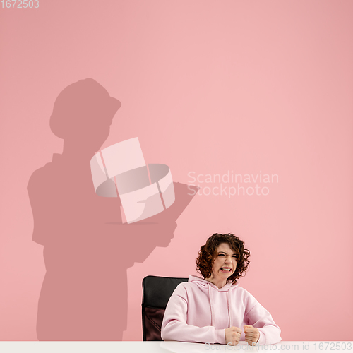 Image of Young woman dreaming about future in big science during her work in office. Becoming a legend. Shadow of dreams on the wall behind her. Copyspace.