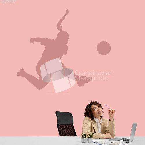 Image of Young woman dreaming about future in big sport during her work in office. Becoming a legend. Shadow of dreams on the wall behind her. Copyspace.