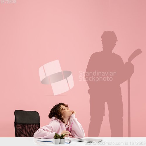 Image of Young woman dreaming about future in big sport during her work in office. Becoming a legend. Shadow of dreams on the wall behind her. Copyspace.