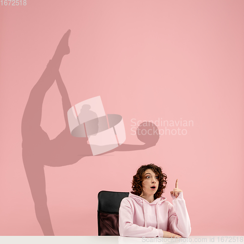 Image of Young woman dreaming about future in big sport during her work in office. Becoming a legend. Shadow of dreams on the wall behind her. Copyspace.