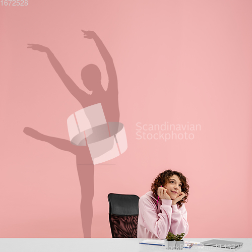 Image of Young woman dreaming about future in big sport during her work in office. Becoming a legend. Shadow of dreams on the wall behind her. Copyspace.