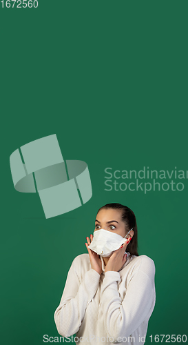 Image of Woman in protective face mask isolated on green studio background. New rules of COVID spreading prevention