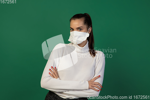 Image of Woman in protective face mask isolated on green studio background. New rules of COVID spreading prevention