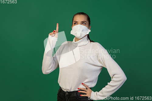 Image of Woman in protective face mask isolated on green studio background. New rules of COVID spreading prevention