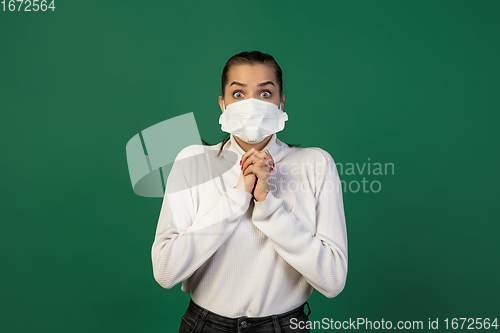 Image of Woman in protective face mask isolated on green studio background. New rules of COVID spreading prevention