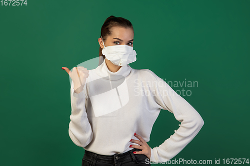 Image of Woman in protective face mask isolated on green studio background. New rules of COVID spreading prevention