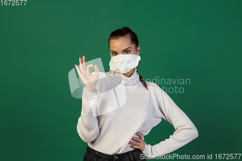 Image of Woman in protective face mask isolated on green studio background. New rules of COVID spreading prevention