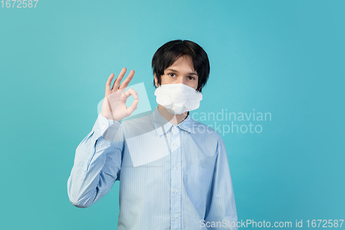 Image of Man in protective face mask isolated on blue studio background. New rules of COVID spreading prevention