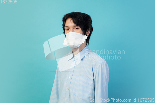 Image of Man in protective face mask isolated on blue studio background. New rules of COVID spreading prevention