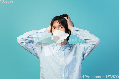 Image of Man in protective face mask isolated on blue studio background. New rules of COVID spreading prevention