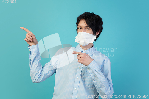 Image of Man in protective face mask isolated on blue studio background. New rules of COVID spreading prevention