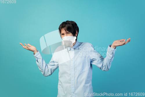 Image of Man in protective face mask isolated on blue studio background. New rules of COVID spreading prevention