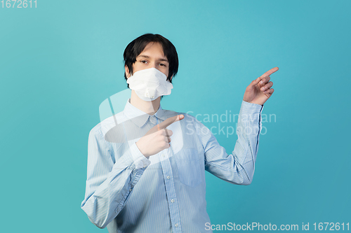 Image of Man in protective face mask isolated on blue studio background. New rules of COVID spreading prevention