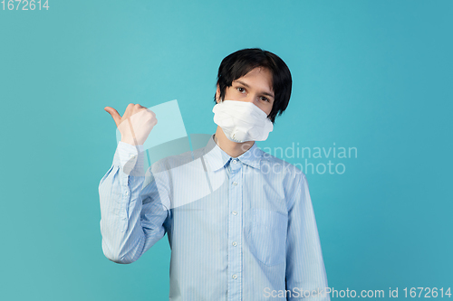 Image of Man in protective face mask isolated on blue studio background. New rules of COVID spreading prevention