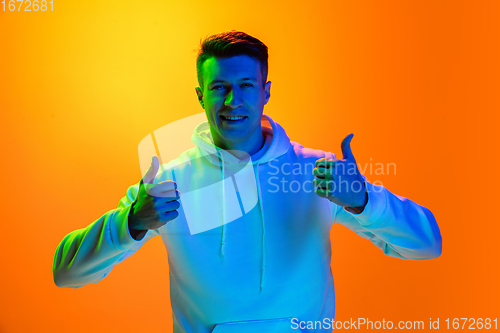 Image of Caucasian beautiful man\'s portrait isolated on yellow studio background in multicolored neon light