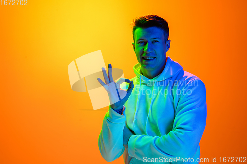 Image of Caucasian beautiful man\'s portrait isolated on yellow studio background in multicolored neon light