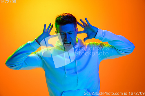 Image of Caucasian beautiful man\'s portrait isolated on yellow studio background in multicolored neon light