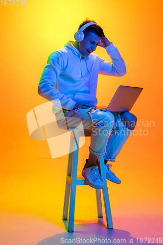 Image of Caucasian beautiful man\'s portrait isolated on yellow studio background in multicolored neon light