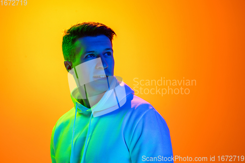 Image of Caucasian beautiful man\'s portrait isolated on yellow studio background in multicolored neon light